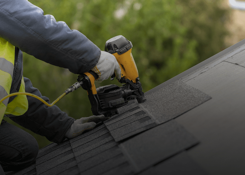 Roofer using nail gun on shingles