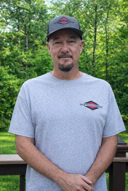 Man in a gray t-shirt and cap outdoors.