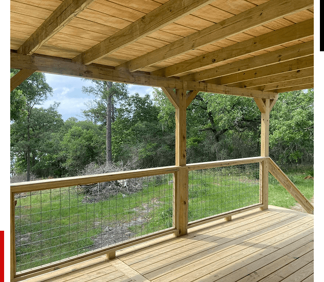 Wooden porch overlooking a green yard with trees and a wire fence.