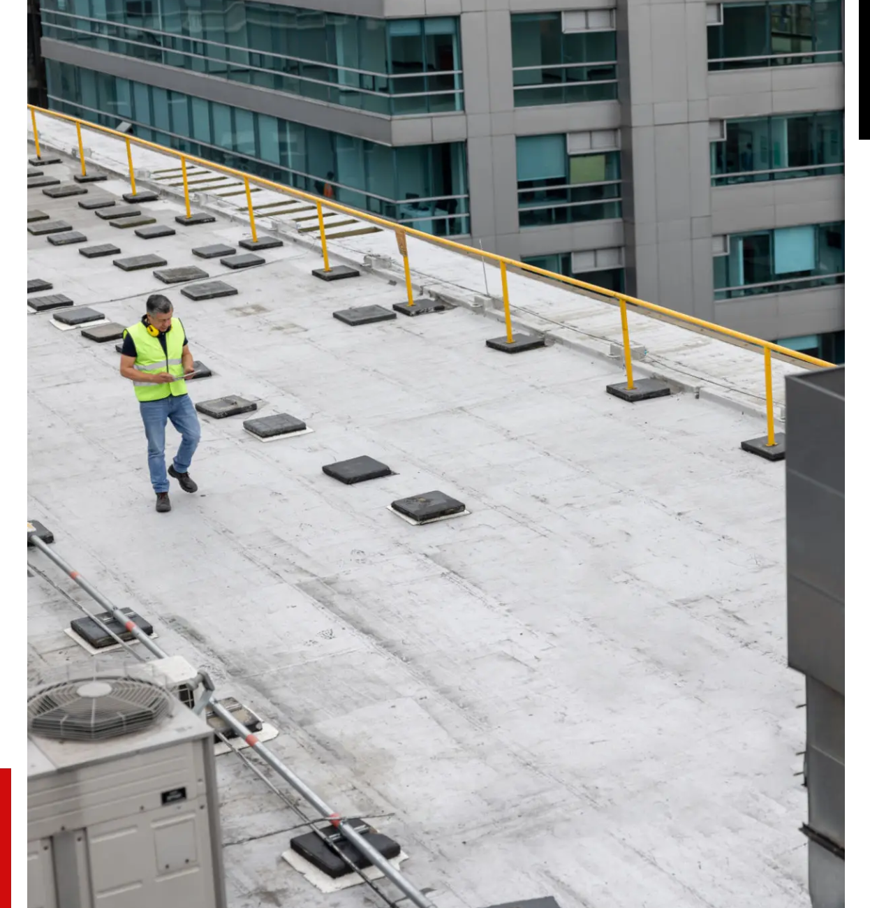 Worker inspecting a rooftop with safety railings in an urban setting.